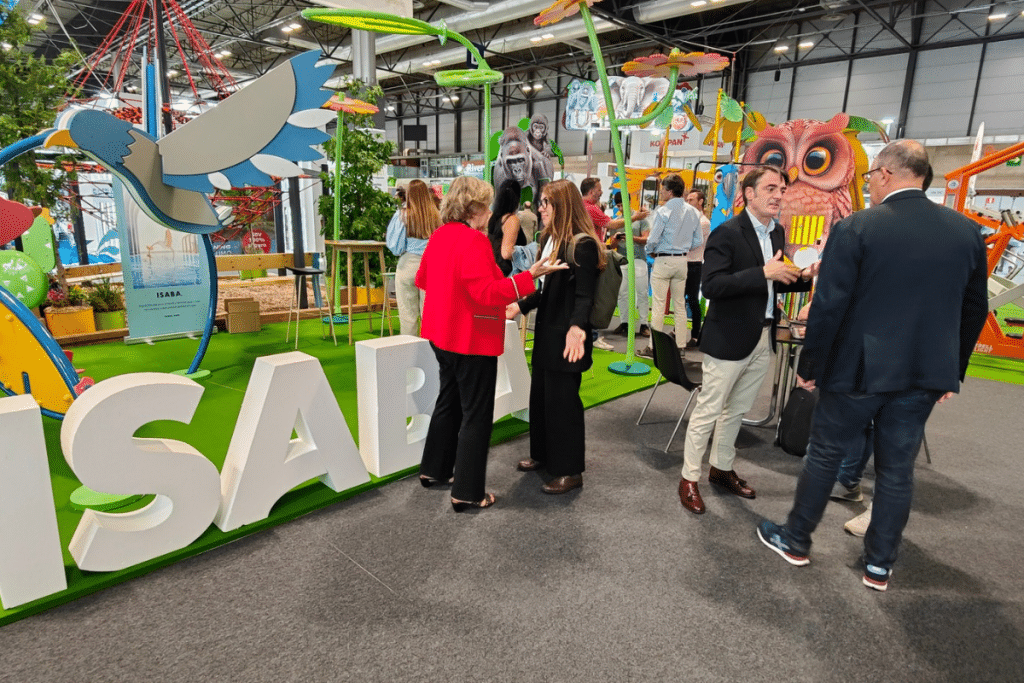 Profesionales conversando en el stand de ISABA durante la feria TECMA, rodeados de estructuras de juego infantil y equipamientos para parques y espacios públicos.
