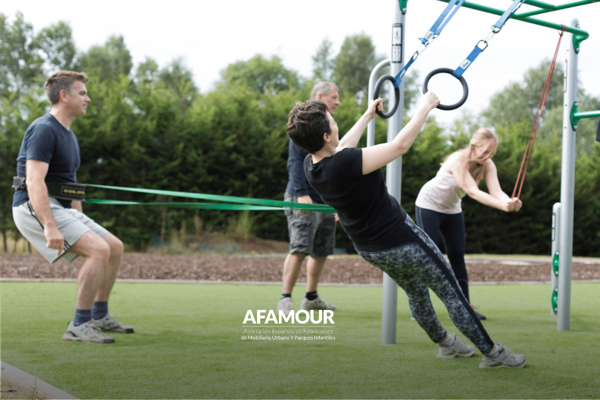 Grupo de adultos realizando ejercicios de fuerza y entrenamiento funcional con anillas y bandas elásticas en un área deportiva al aire libre.