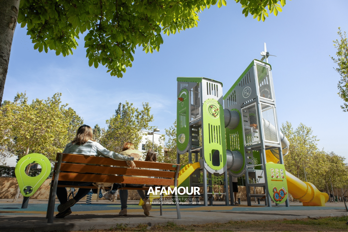 Parque infantil al aire libre con estructuras de juego verdes, toboganes y plataformas de distintas alturas, rodeado de árboles.