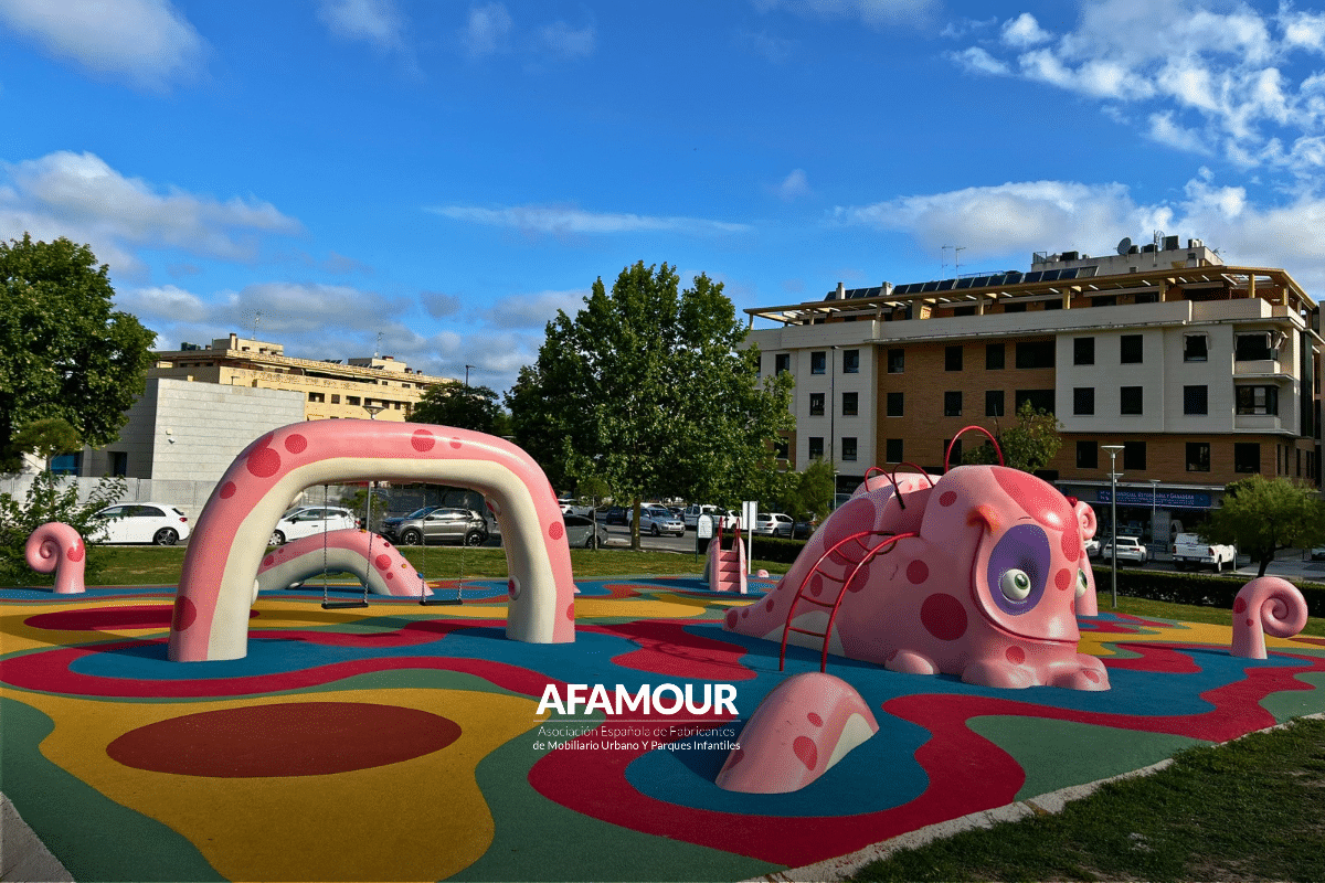 Parque infantil urbano con estructuras de juego de formas orgánicas y pavimento de seguridad multicolor.