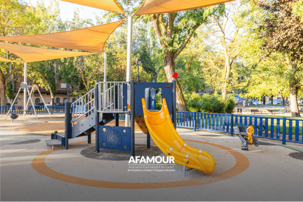 Parque infantil con tobogán amarillo y estructuras de juego protegidas por toldos de sombra para mejorar el confort climático en espacios públicos.