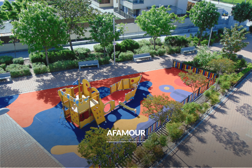 Vista aérea de un parque infantil con juegos, pavimento de colores, árboles y zonas verdes que contribuyen al confort climático del espacio público.