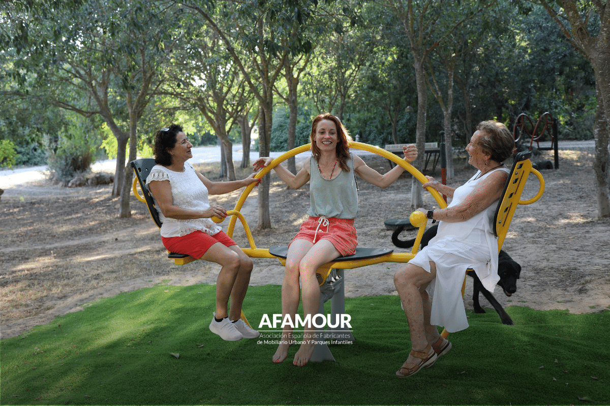 Tres mujeres de diferentes edades utilizan un equipamiento de ejercicio al aire libre en un parque, ejemplo de espacio público intergeneracional.