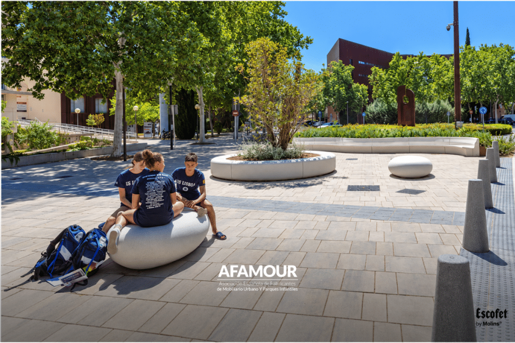 Plaza pública arbolada con bancos de diseño, jardineras y zonas de descanso donde varios jóvenes disfrutan de un espacio urbano de convivencia.