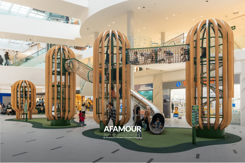Zona de juegos infantiles en un centro comercial con estructuras de madera, redes de trepa, puentes y toboganes para el ocio de los niños.